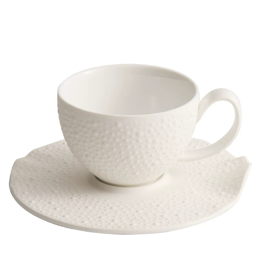 White textured ceramic cup with latte art on an irregular dotted saucer