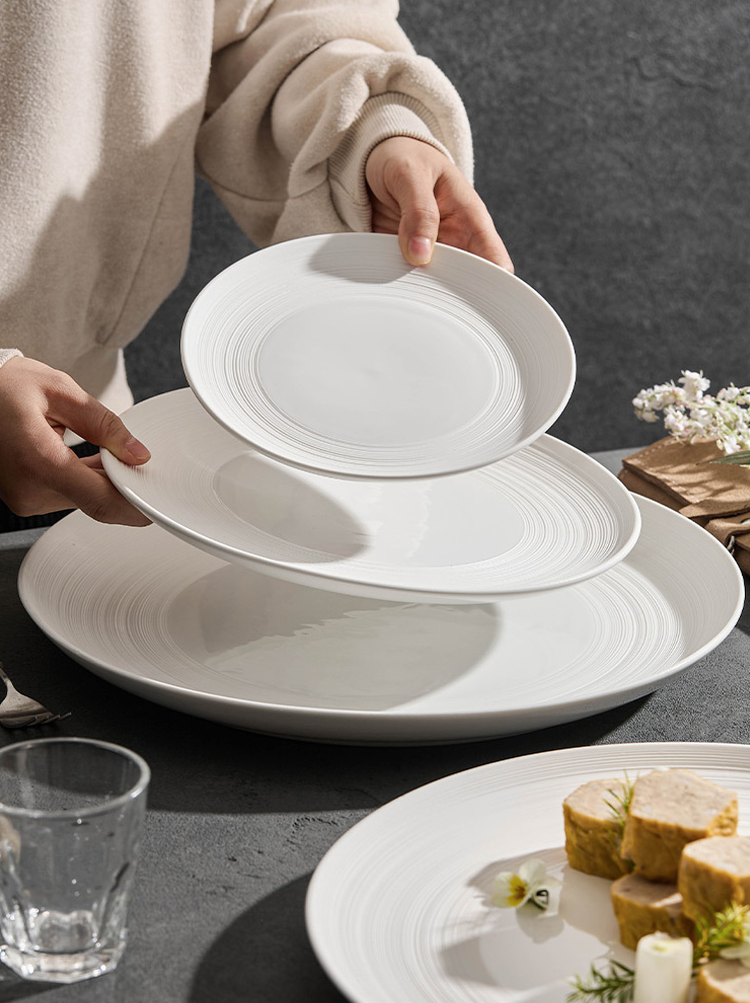 White ceramic dinner plate with fine concentric lines and a plated terrine