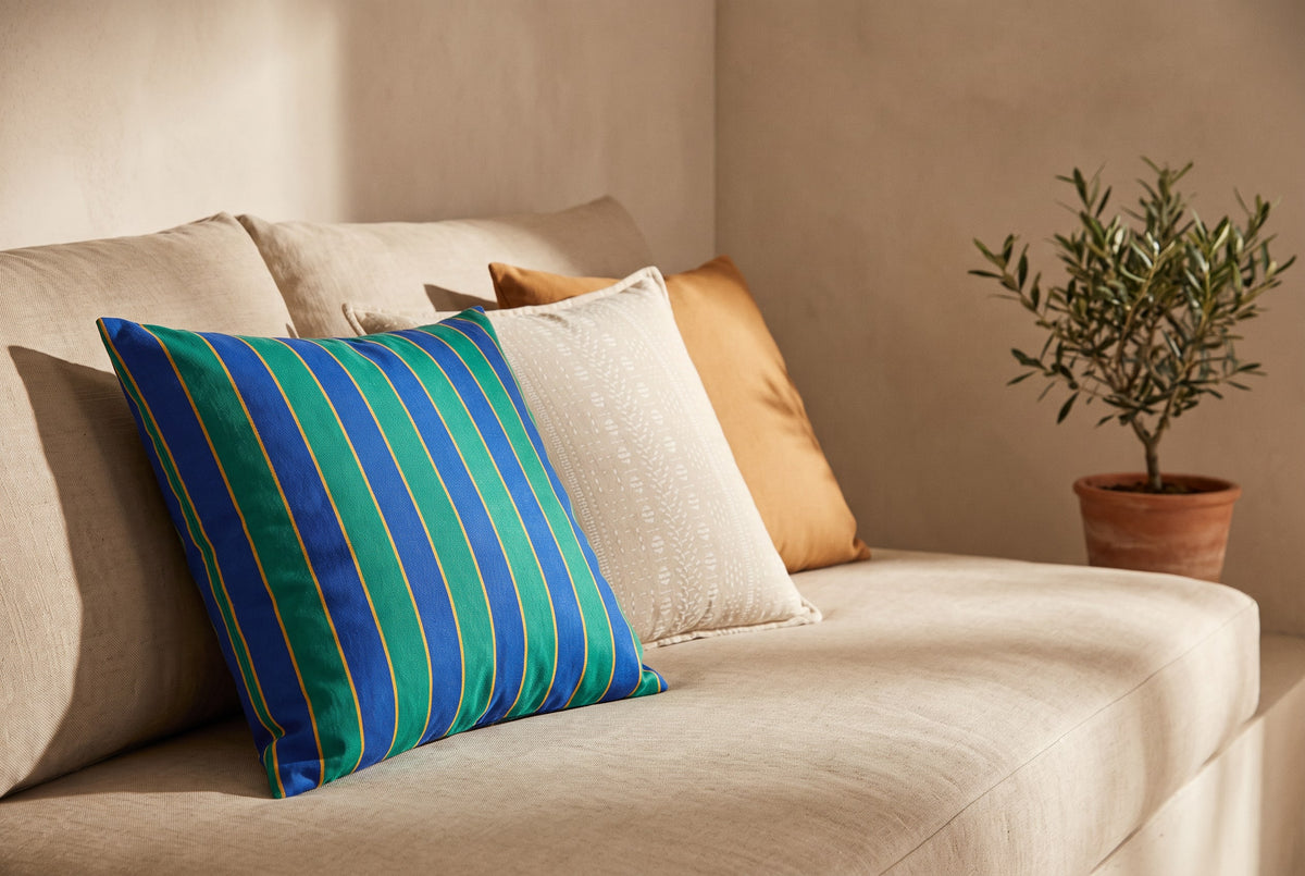 Striped canvas cushion with stone and caramel cushions on a linen sofa beside an olive tree