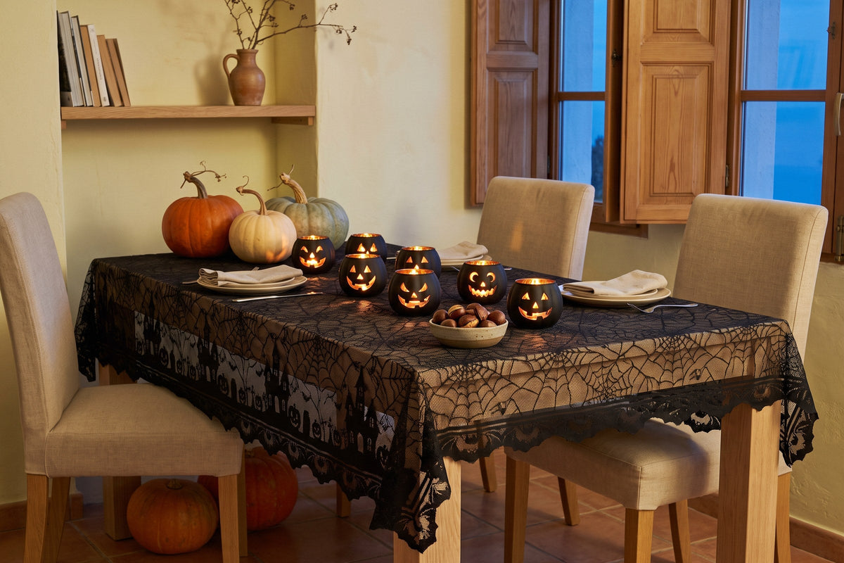 Halloween dinner table in a small Mediterranean flat at dusk: black lace spider web tablecloth, lit pumpkin glass candle holders, chestnuts and real pumpkins