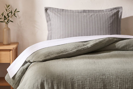 Lark muslin duvet cover in eucalyptus turned back over a white sheet beside a grey pinstripe pillow