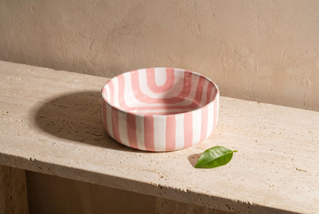Pink and white radiating-stripe ceramic bowl with a citrus leaf on a stone ledge