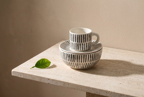 Striped ceramic espresso cup and saucer resting on a matching bowl with a citrus leaf