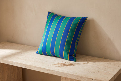 Blue and green striped canvas cushion propped on a stone bench with a dried grass stem