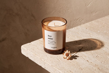 Unlit Bee Mine scented candle with a dried flower on a stone ledge