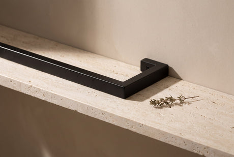 Matte black square-profile steel towel rail section with a dried herb sprig