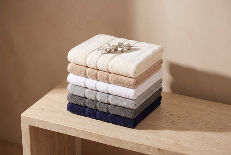 Stack of folded hotel-luxury towels in six colours with a eucalyptus sprig