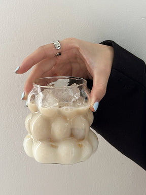 Clear grape-shaped glass cup with a handle holding iced coffee