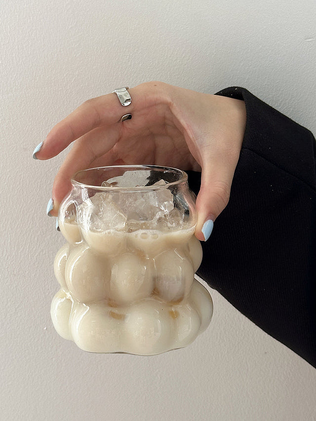 Clear grape-shaped glass cup with a handle holding iced coffee