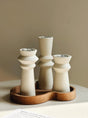 Three cream unglazed ceramic candle holders of different heights on a wooden tray