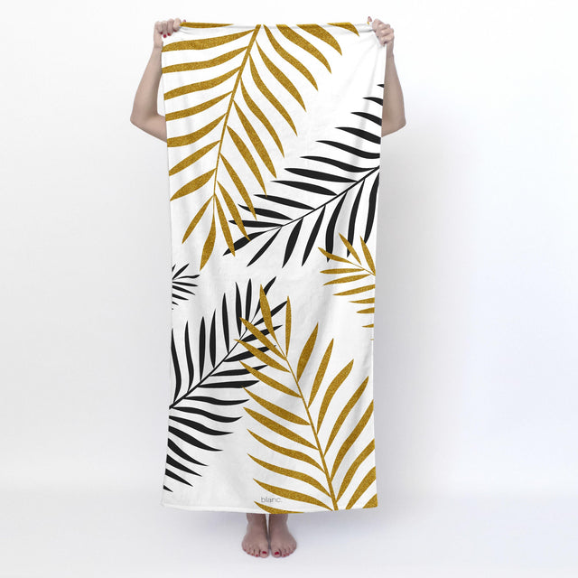 White beach towel printed with gold and black palm leaves