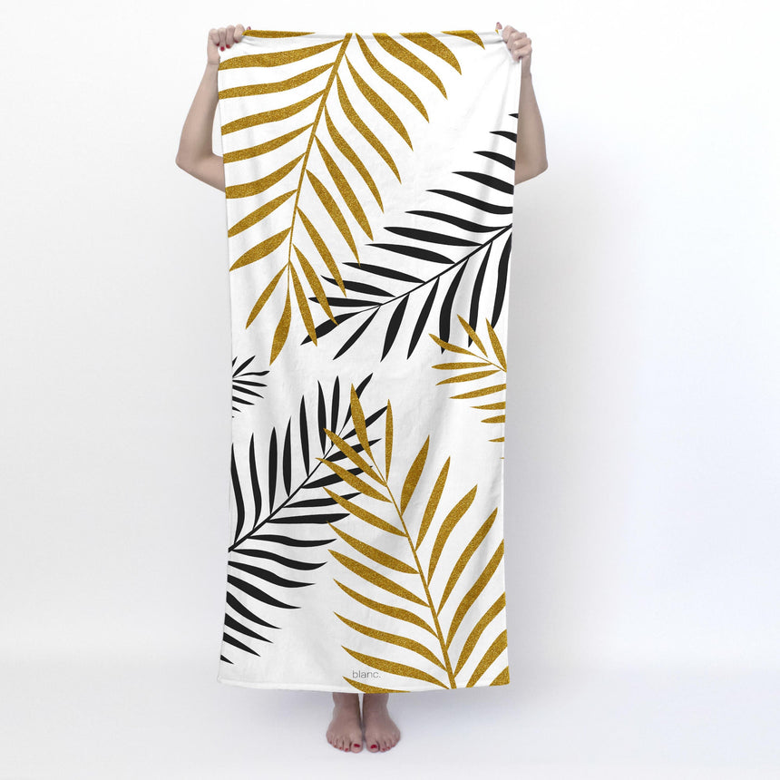 White beach towel printed with gold and black palm leaves