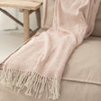 Pink woven throw with a cream fringe on a beige sofa