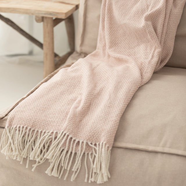 Pink woven throw with a cream fringe on a beige sofa