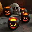Black glass pumpkin face candle holders lit with candles beside a skull