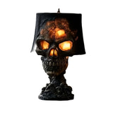 Black resin skull table lamp with glowing orange eyes and a cracked lava finish under a black shade