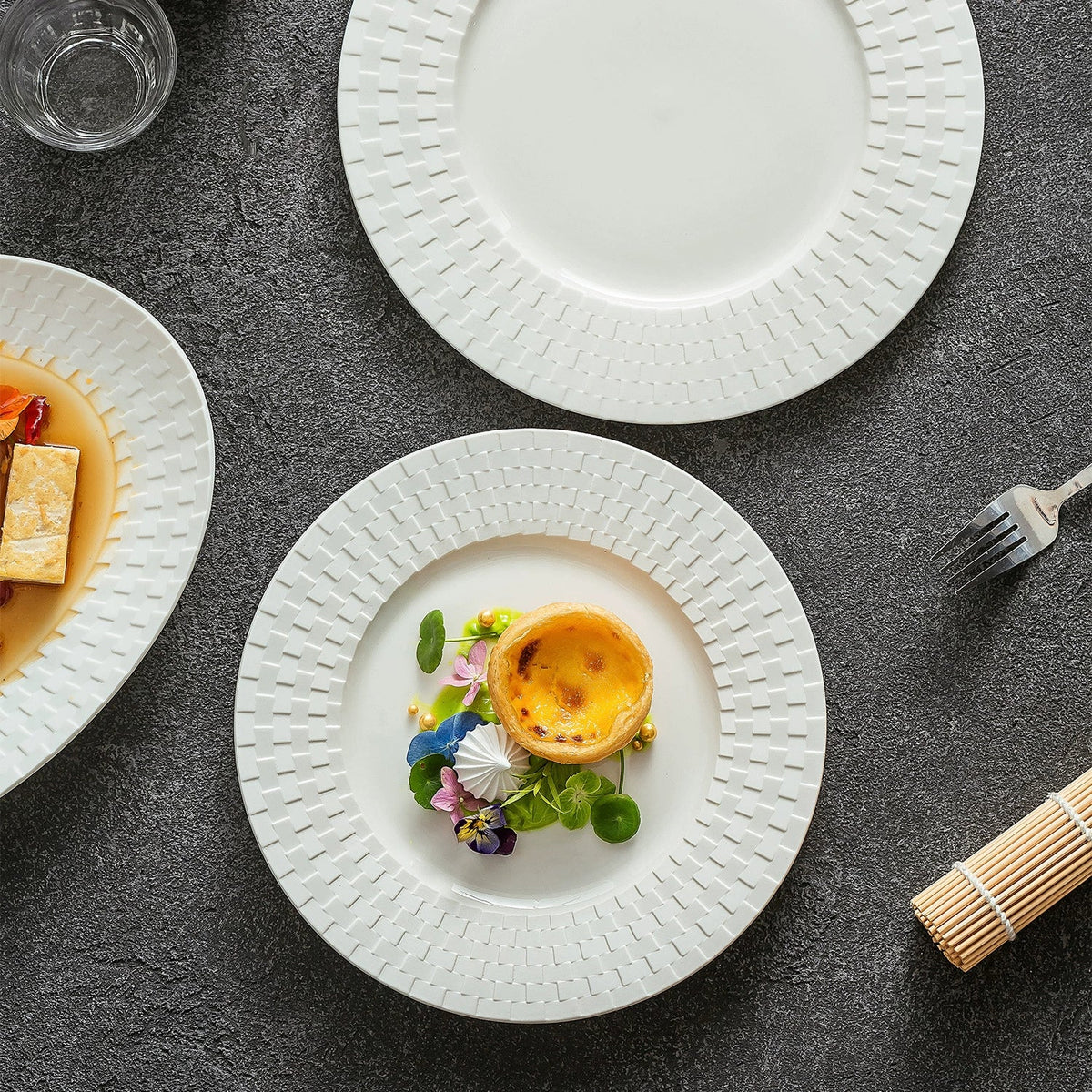 White ceramic plate with an embossed woven rim holding a custard tart