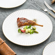 White pleated porcelain plate with a thin gold rim holding a lamb chop