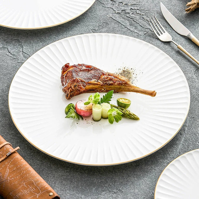 White pleated porcelain plate with a thin gold rim holding a lamb chop