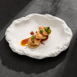 White matte ceramic plate with a rough rock-textured rim holding a plated fish dish