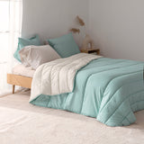 Reversible quilted comforter in mint and cream on a bed