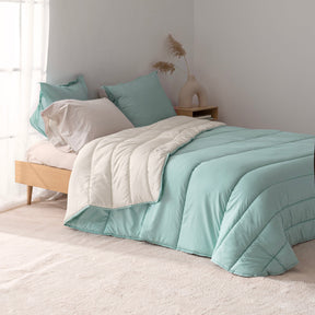 Reversible quilted comforter in mint and cream on a bed