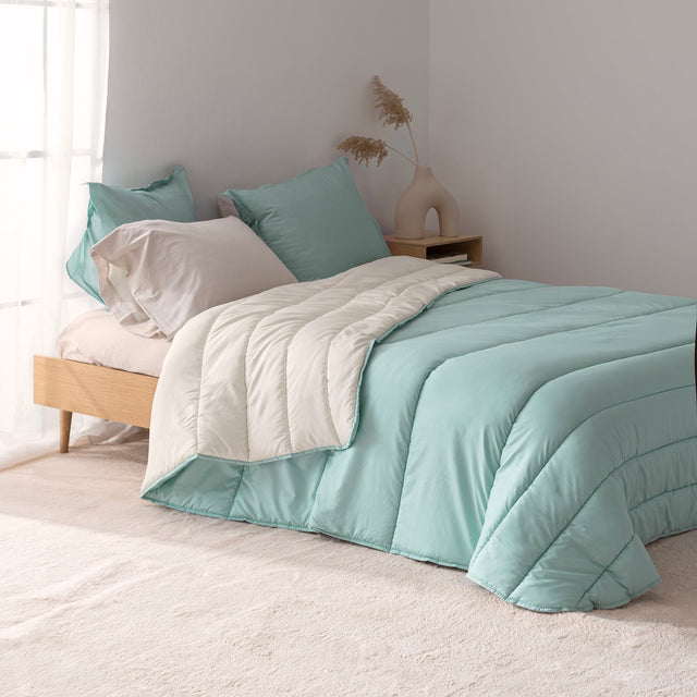 Reversible quilted comforter in mint and cream on a bed