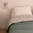 Reversible quilted comforter in sage green and cream on a bed