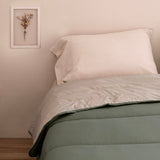 Reversible quilted comforter in sage green and cream on a bed