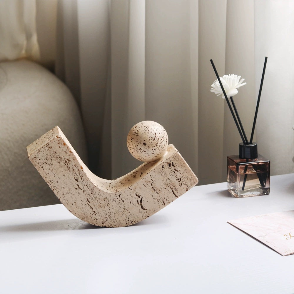 Sand-coloured pitted stone sculpture of a sphere resting on a curved arc