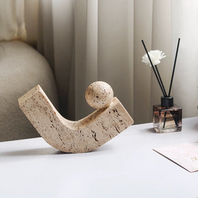 Sand-coloured pitted stone sculpture of a sphere resting on a curved arc