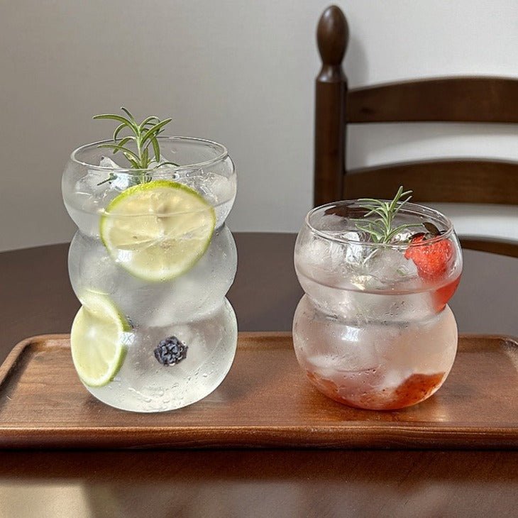 Two clear bubble-shaped glass tumblers with lime, strawberry and rosemary