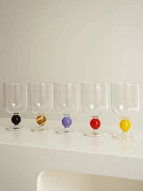 Five clear wine glasses in a row, front-on, each with a different coloured gumball stem