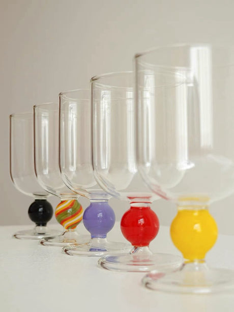 Five clear wine glasses in a row, each with a differently coloured gumball stem