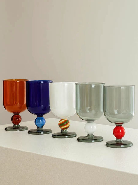 Five wine glasses in solid colours side by side: amber, blue, white and two in smoke grey