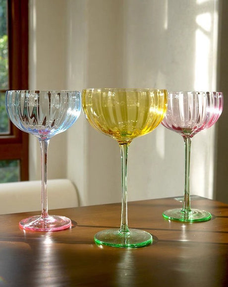 Three hand-blown pastel coupe glasses with ribbed bowls on a wooden table