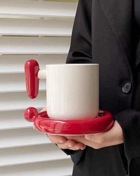 Cream ceramic mug with a red handle on a red round saucer