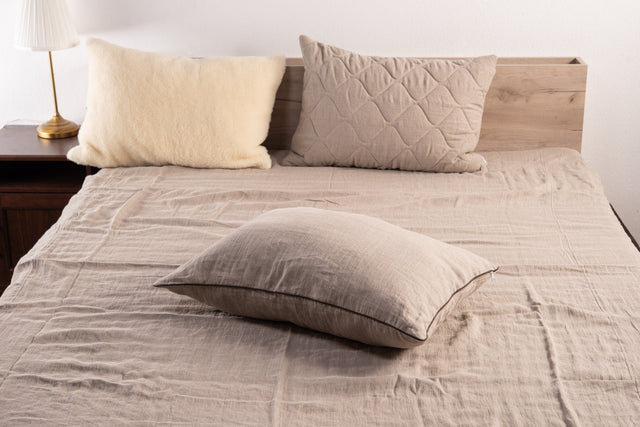 Natural linen pillow with brown edging on a linen-covered bed