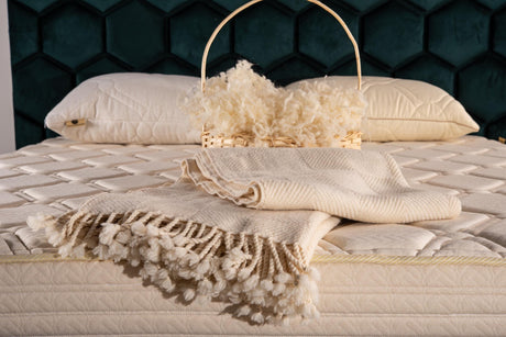 Undyed merino wool throw on a bed beside a basket of raw wool