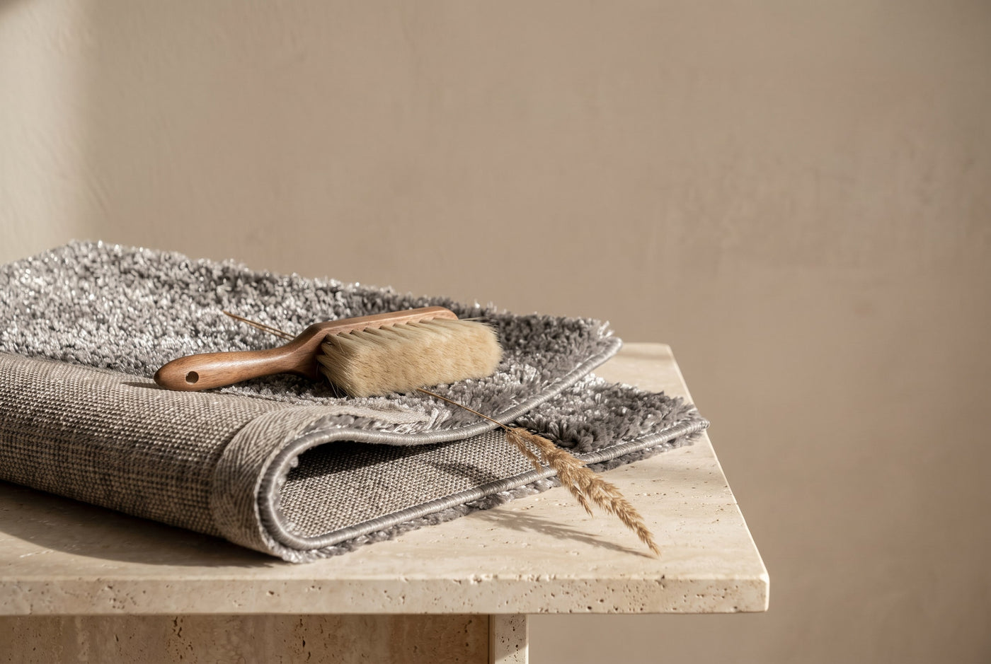 Folded corner of a grey high-pile polyester rug with a soft brush and dried grass
