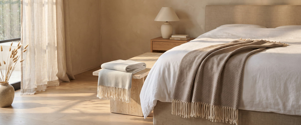Bedroom with a taupe fringed throw across the foot of the bed and a pale grey throw folded on a travertine bench
