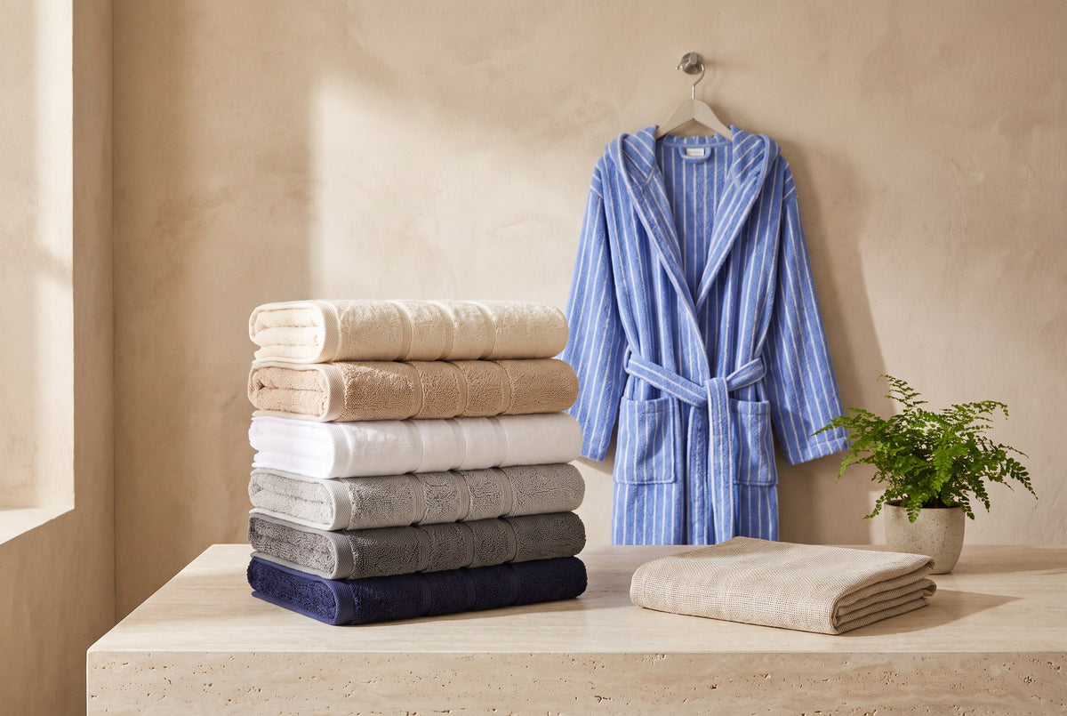 Stacked towels, a striped hooded robe hung on a hook and a linen towel beside a fern