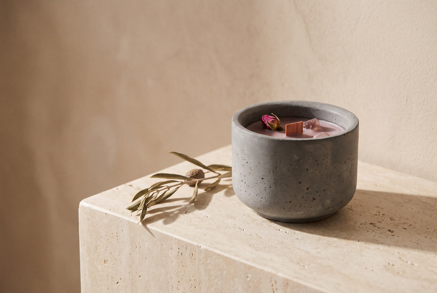 Candle in a mauve cast-concrete vessel with dried rosebuds and an olive sprig