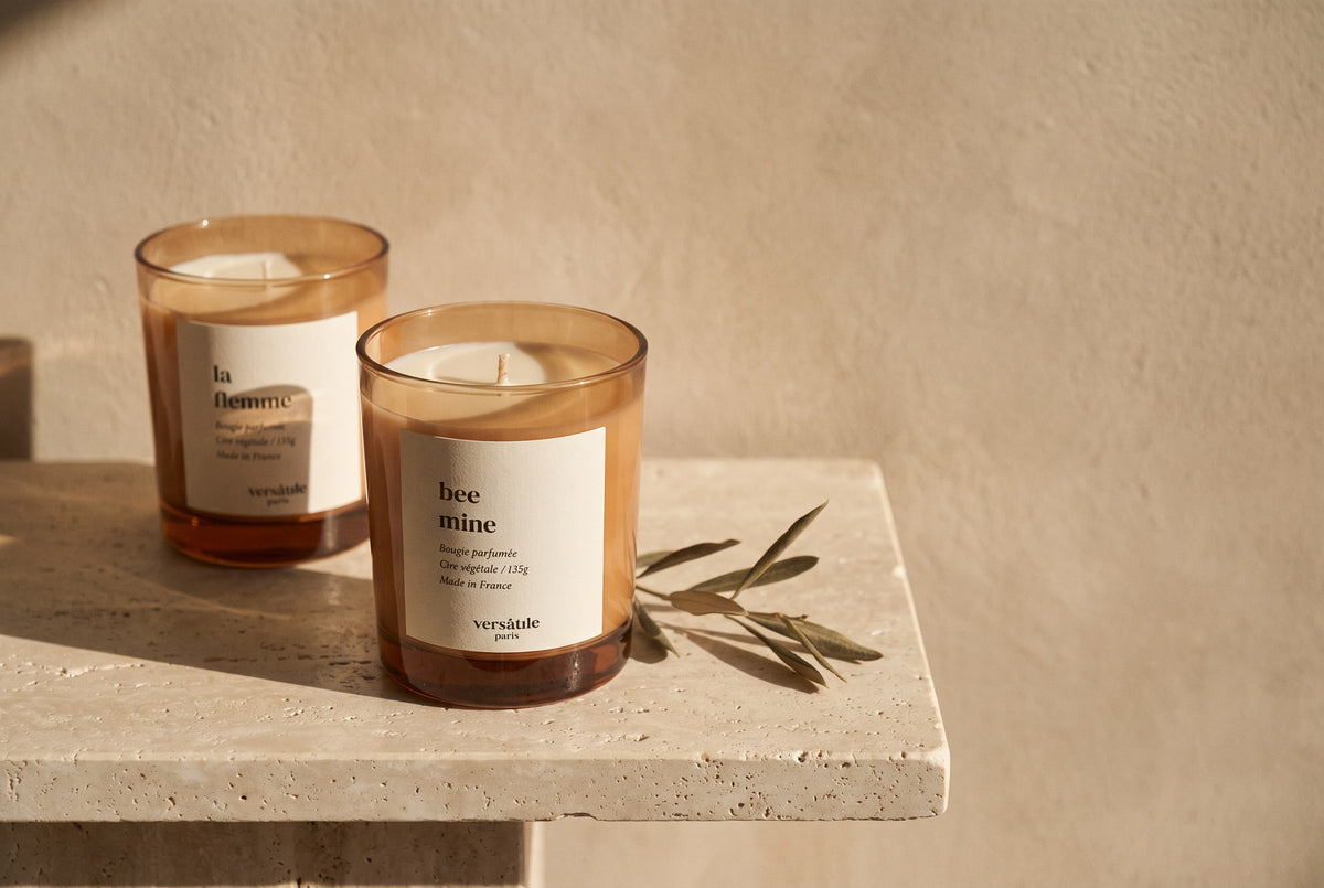Bee Mine and La Flemme scented candles beside an olive sprig on a stone ledge